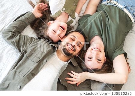 Happy family at home. Mother father children daughter relaxing in bed at home indoor. Mom dad parents kid girl relax playing hugging having fun together. Family smiling laughing enjoying tender moment 138910285