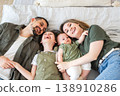 Happy family at home. Mother father two children daughters relaxing in bed indoor. Mom dad parents kids girls relax playing hugging having fun together. Family smiling laughing enjoying tender moment 138910286