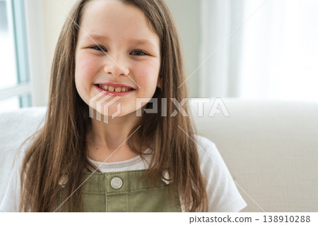 Happy girl at home. Smiling cute little brown haired Caucasian girl looking at camera. Portrait of happy female child at home. Smiling face of 10 year old girl looking at camera 138910288