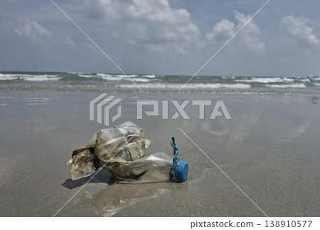 Ocean's Unwanted Guest: A weathered plastic bottle lies stranded on the sandy shore, a stark reminder of environmental pollution and the urgent need for conservation. 138910577