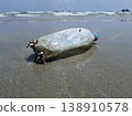 Ocean's Unwanted Guest: A weathered plastic bottle lies stranded on the sandy shore, a stark reminder of environmental pollution and the urgent need for conservation. 138910578
