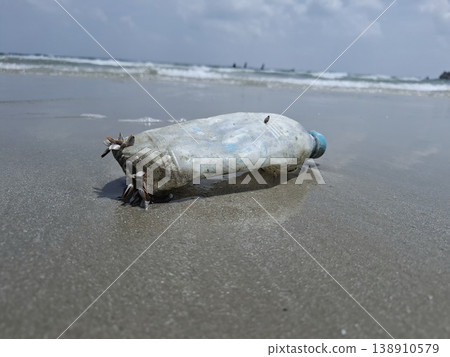 Ocean's Unwanted Guest: A weathered plastic bottle lies stranded on the sandy shore, a stark reminder of environmental pollution and the urgent need for conservation. 138910579