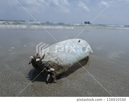 Ocean's Unwanted Guest: A weathered plastic bottle lies stranded on the sandy shore, a stark reminder of environmental pollution and the urgent need for conservation. 138910580