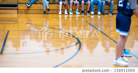 Basketball players prepare for the game in a gym during a youth sports event with fans in the background and a polished wooden floor Basketball players prepare for the game in a gym during a youth sports event with fans in the background and a polished wooden floor 138911009