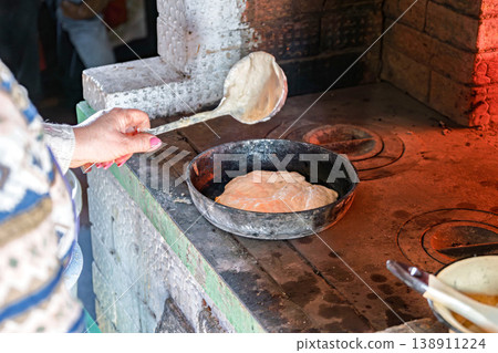 Baker creates bread in wood-burning oven as part of traditional cooking in a kitchen Baker creates bread in wood-burning oven as part of traditional cooking in a kitchen 138911224