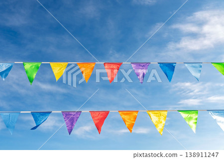 Colorful festive pennant flags hanging under bright wispy clouds sky Colorful festive pennant flags hanging under bright wispy clouds sky 138911247