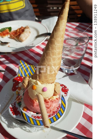 Colorful ice cream dessert featuring a cone, candy decorations, and a playful design served on a decorative plate Colorful ice cream dessert featuring a cone, candy decorations, and a playful design served on a decorative plate 138911249