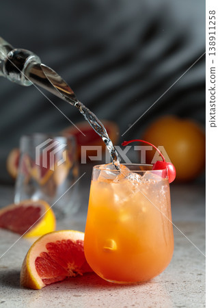 Strong alcohol is poured into a glass with ice and grapefruit juice. Strong alcohol is poured into a glass with ice and grapefruit juice. 138911258