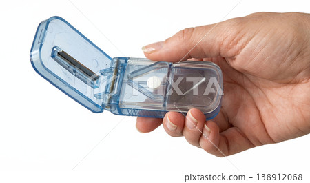 Hand holding compact plastic pill splitter and storage container with built-in blade and compartments, representing medication management and dosage accuracy Hand holding compact plastic pill splitter and storage container with built-in blade and compartments, representing medication management and dosage accuracy 138912068
