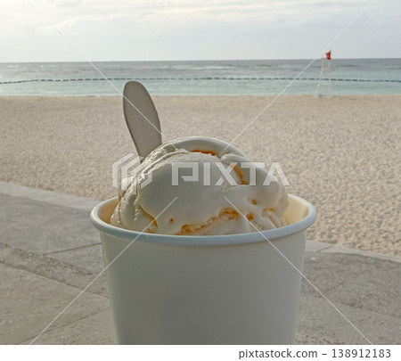 Creamy vanilla ice cream in a cup with a wooden spoon on a sandy beach Creamy vanilla ice cream in a cup with a wooden spoon on a sandy beach 138912183
