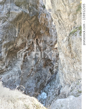 Mountain river flowing through a stone crevice, North Ossetia, Russia, bright summer day. Clear water rushing between narrow rocky walls under sunlight Mountain river flowing through a stone crevice, North Ossetia, Russia, bright summer day. Clear water rushing between narrow rocky walls under sunlight 138912205
