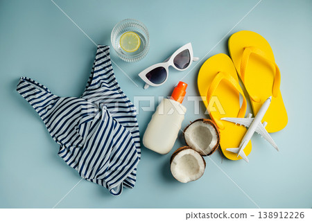 Summer background, beach accessories, swimm suit, sun glasses, airplane and flip flops on blue background. Summer holiday background flat lay Summer background, beach accessories, swimm suit, sun glasses, airplane and flip flops on blue background. Summer holiday background flat lay 138912226