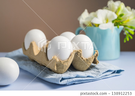 Easter eggs background. White eggs in cardboard box and freesias flowers in a vase. Spring holiday Easter eggs background. White eggs in cardboard box and freesias flowers in a vase. Spring holiday 138912253