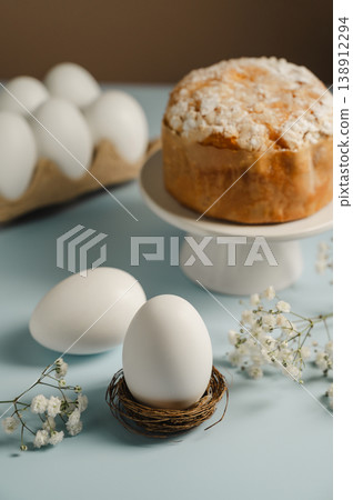 Easter white egg in the nest and easter cake with gypsophila white flower. Spring holidays background Easter white egg in the nest and easter cake with gypsophila white flower. Spring holidays background 138912294