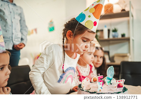 Children celebrate a birthday with a cake and party hats in a room with decorations and friends around in the afternoon Children celebrate a birthday with a cake and party hats in a room with decorations and friends around in the afternoon 138912771
