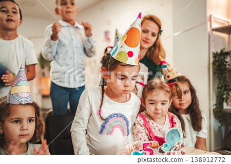 Kids enjoy birthday celebration with cake and fun in a colorful room with decorations and friends singing Kids enjoy birthday celebration with cake and fun in a colorful room with decorations and friends singing 138912772