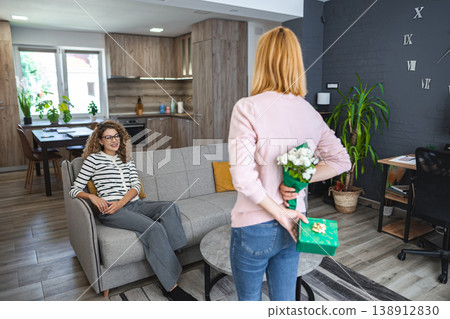 Blonde smiling woman surprises her best friend with a gift and flowers Blonde smiling woman surprises her best friend with a gift and flowers 138912830