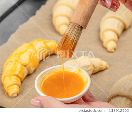 Brushing croissants with egg wash before baking, close up Brushing croissants with egg wash before baking, close up 138912903