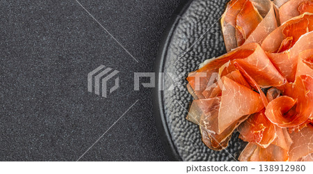 Overhead view of sliced cured ham on a black plate with copy space for gourmet food advertising Overhead view of sliced cured ham on a black plate with copy space for gourmet food advertising 138912980