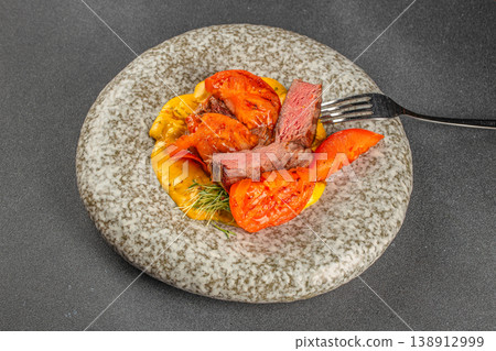 Cut grilled pork steak with tomato and sauce on plate top view Cut grilled pork steak with tomato and sauce on plate top view 138912999