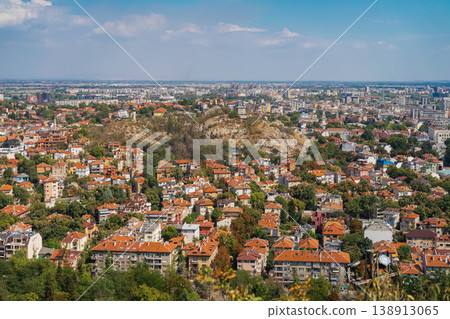 Panoramic cityscape aerial view of Plovdiv with residential buildings, red tile roofs, rocky hill in urban district under blue sky. Plovdiv skyline and architecture. Bulgarian travel destination Panoramic cityscape aerial view of Plovdiv with residential buildings, red tile roofs, rocky hill in urban district under blue sky. Plovdiv skyline and architecture. Bulgarian travel destination 138913065