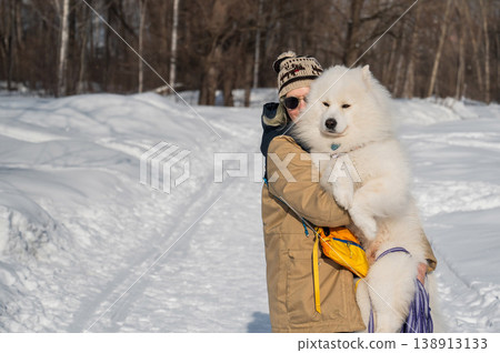 Smiling woman holding fluffy samoyed dog in snowy winter park. Smiling woman holding fluffy samoyed dog in snowy winter park. 138913133