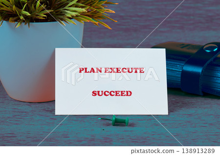 A white business card with the words Plan Execute Succeed in red is displayed upright on a textured dark teal surface A white business card with the words Plan Execute Succeed in red is displayed upright on a textured dark teal surface 138913289