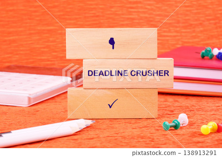 Three wooden blocks stacked on an orange desk, displaying DEADLINE CRUSHER with a thumbs down and a checkmark 138913291