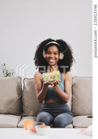 Young nutritionist showing bell peppers during an online video call consulting about healthy eating, sitting at home at a table with vegetables, laptop and measuring tape 138913346