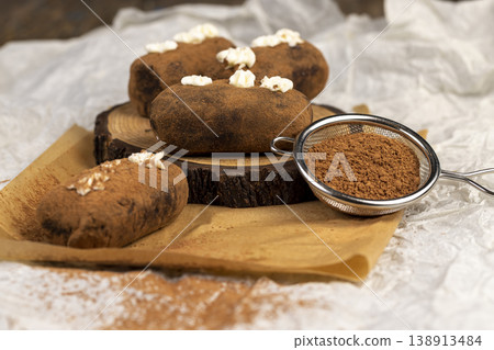sweet brown pastry potatoes are lying on a serving board and paper, sweet classic cake from butter and a large amount of cocoa mixed with sponge cake and cognac, cocoa powder is scattered nearby sweet brown pastry potatoes are lying on a serving board and paper, sweet classic cake from butter and a large amount of cocoa mixed with sponge cake and cognac, cocoa powder is scattered nearby 138913484