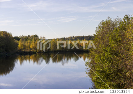 autumn lake in sunny weather at sunset, beautiful deciduous trees on the riverbank before the fall of leaves, evening before sunset autumn lake in sunny weather at sunset, beautiful deciduous trees on the riverbank before the fall of leaves, evening before sunset 138913534