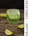 one cold lime-flavored carbonated drink with lots of gas bubbles and whole pieces of fresh sour lime, sweet green-colored carbonated drink poured into a glass with ice 138913550