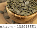 a large number of peeled green large dried pumpkin seeds are on a wooden walnut board and in wooden dishes, a large number of healthy large pumpkin seeds without shells 138913551