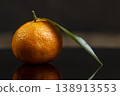 one fresh orange small tangerine with green leaves are reflected on a black mirror , a group of ripe sweet tangerines with green leaves with reflection on a black glass 138913553