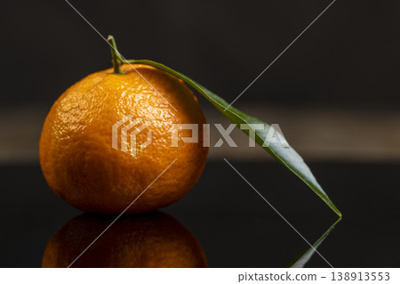 one fresh orange small tangerine with green leaves are reflected on a black mirror , a group of ripe sweet tangerines with green leaves with reflection on a black glass one fresh orange small tangerine with green leaves are reflected on a black mirror , a group of ripe sweet tangerines with green leaves with reflection on a black glass 138913553