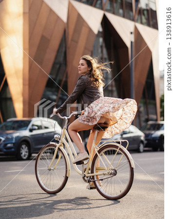 Young woman cycling on city street on a windy day Young woman cycling on city street on a windy day 138913616
