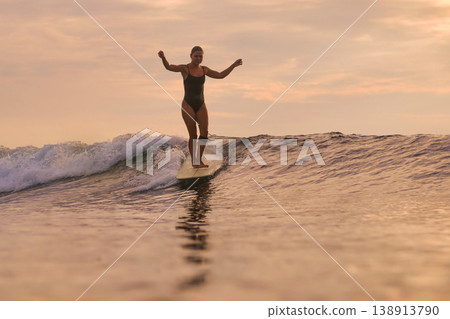 Athletic Female Surfer Displaying Power And Poise On Sunset Ocean Wave Athletic Female Surfer Displaying Power And Poise On Sunset Ocean Wave 138913790