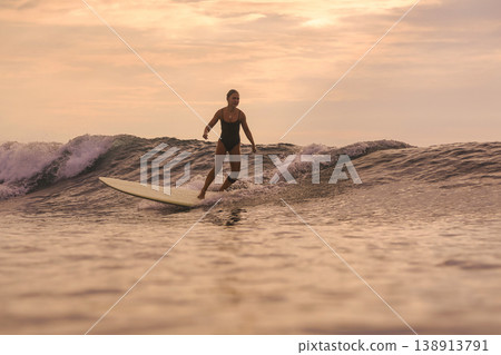 Woman Joyfully Dances Atop Surfboard During Sunset Amidst Gentle Waves Woman Joyfully Dances Atop Surfboard During Sunset Amidst Gentle Waves 138913791