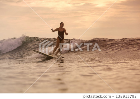 Athletic Female Surfer Displaying Power And Poise On Sunset Ocean Wave Athletic Female Surfer Displaying Power And Poise On Sunset Ocean Wave 138913792