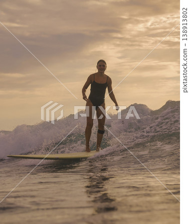 Athletic Woman Expertly Balancing On Surfboard At Dusk Amid Ocean Spray Athletic Woman Expertly Balancing On Surfboard At Dusk Amid Ocean Spray 138913802