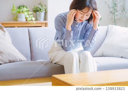 A middle-aged woman clutches her temples due to a headache. A middle-aged woman clutches her temples due to a headache. 138913821