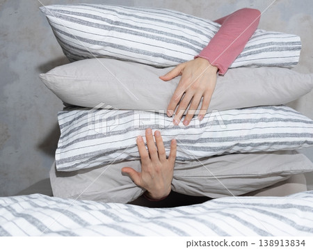 woman holds stack of pillows with her hands while sitting on the bed. rest and restful sleep. woman holds stack of pillows with her hands while sitting on the bed. rest and restful sleep. 138913834
