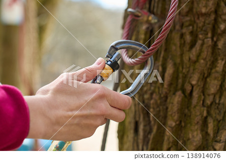 Close up of hand attaching metal carabiner to steel safety cable around tree 138914076