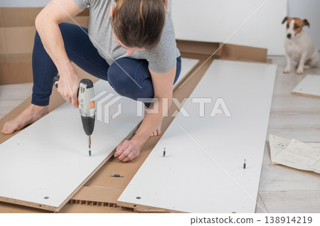 A Caucasian woman uses a screwdriver to tighten a screw while assembling a cabinet. 138914219