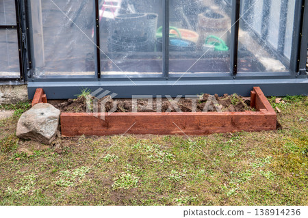 Preparing Wooden Raised Garden Bed Along Greenhouse Wall in Backyard Preparing Wooden Raised Garden Bed Along Greenhouse Wall in Backyard 138914236