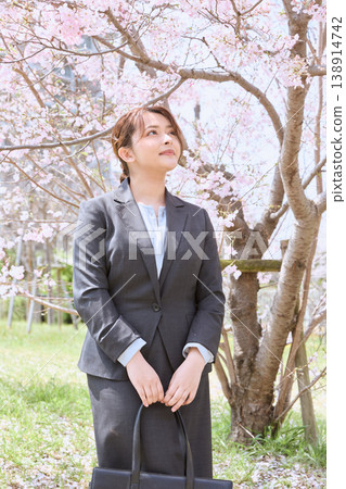 A young woman in a business suit carrying a business bag under cherry blossoms – an image of spring job hunting. A young woman in a business suit carrying a business bag under cherry blossoms – an image of spring job hunting. 138914742
