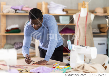 Middle-aged male dressmaker sketching clothing pattern in sewing workshop Middle-aged male dressmaker sketching clothing pattern in sewing workshop 138915745