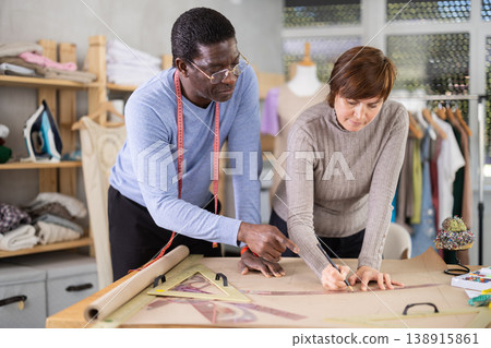 Two sewing workshop workers draw patterns on paper Two sewing workshop workers draw patterns on paper 138915861