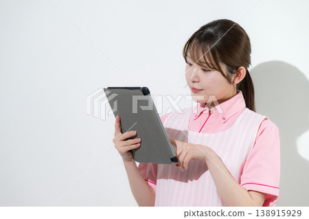 An IT-driven image of a woman working as a caregiver or childcare worker in a home care setting, pointing to a tablet against a white background. An IT-driven image of a woman working as a caregiver or childcare worker in a home care setting, pointing to a tablet against a white background. 138915929