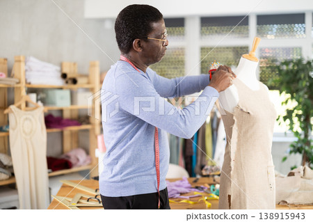 African American man tailor connects parts of dress on mannequin. 138915943